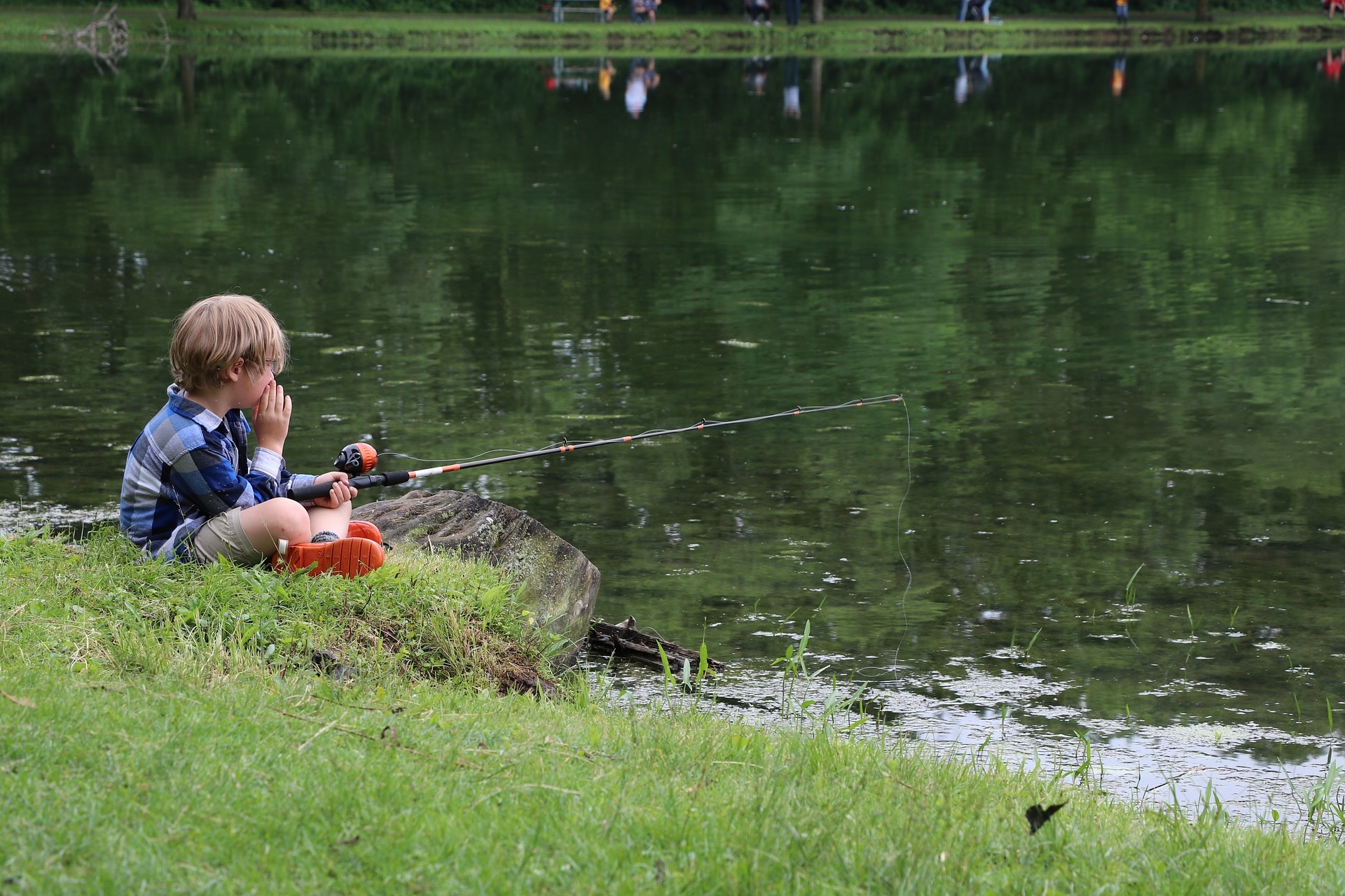 Kind sitzt mit Angel am Weiher